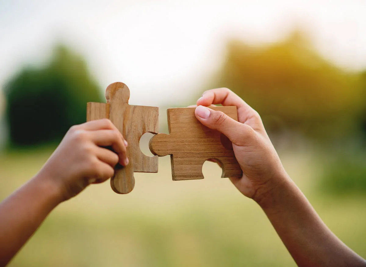 Zwei Puzzleteile, die mit zwei Händen in der Luft zusammengeführt werden
